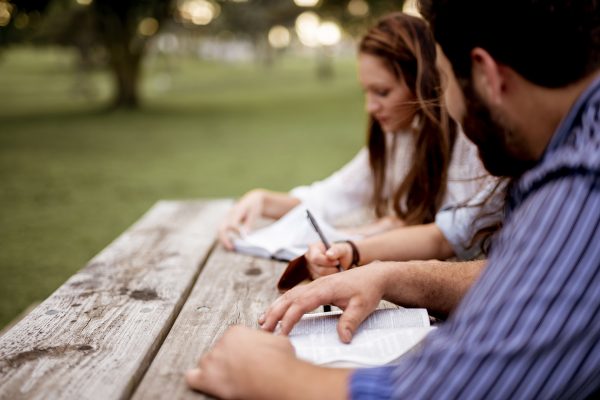 A closeup shot of people sitting in the park and reading the bible with a blurred background